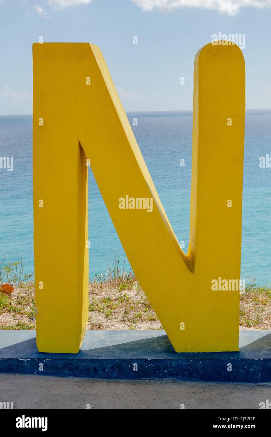 Scultura in calcestruzzo dipinta di giallo di una lettera N con il Mar dei Caraibi sullo sfondo. Foto Stock
