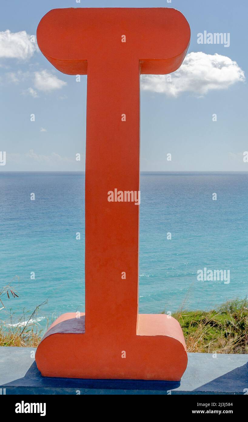 Scultura in calcestruzzo dipinta di rosso di una lettera i con il Mar dei Caraibi sullo sfondo. Foto Stock
