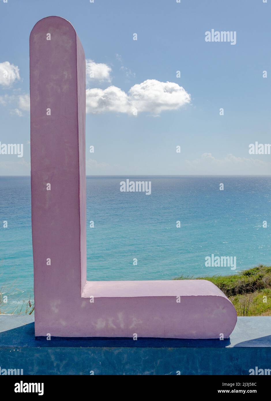 Scultura in calcestruzzo dipinta di viola di una lettera L con il Mar dei Caraibi sullo sfondo. Foto Stock