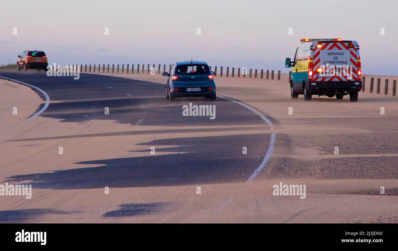 Spagna, Isole Canarie, Fuerteventura, zona delle dune di El Jable, strada coperta da sabbia, autovettura, furgone di manutenzione stradale, luci lampeggianti accese Foto Stock