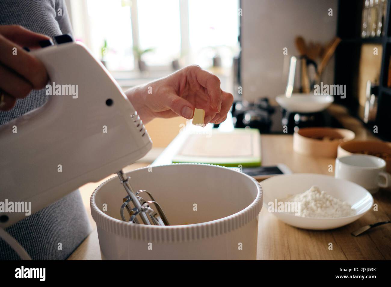 La donna ha le mani che cucinano una torta di gemme in cucina in piedi al banco utilizzando un mixer manuale per frullare gli ingredienti più freschi in un recipiente di miscelazione bianco, gli ingredienti sul tavolo Foto Stock