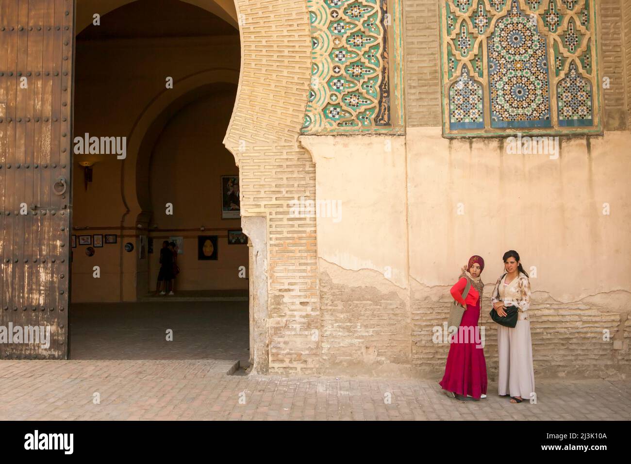 Due giovani donne si trovano accanto a un muro vicino a un ingresso in Marocco; Meknes, Marocco Foto Stock