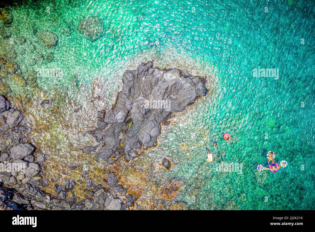 Vista da un drone direttamente sopra i nuotatori nelle limpide acque turchesi dell'Oceano Pacifico lungo la costa frastagliata di Maui, Hawaii, USA Foto Stock