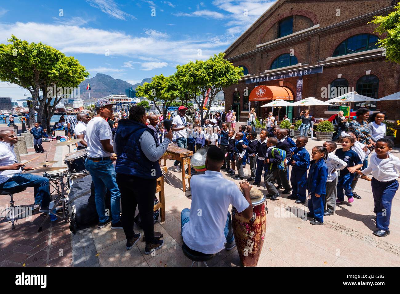 I bambini delle scuole in uniforme si fermano per ascoltare un gruppo musicale di percussioni lungo il lungomare di Città del Capo; Città del Capo, Sudafrica Foto Stock