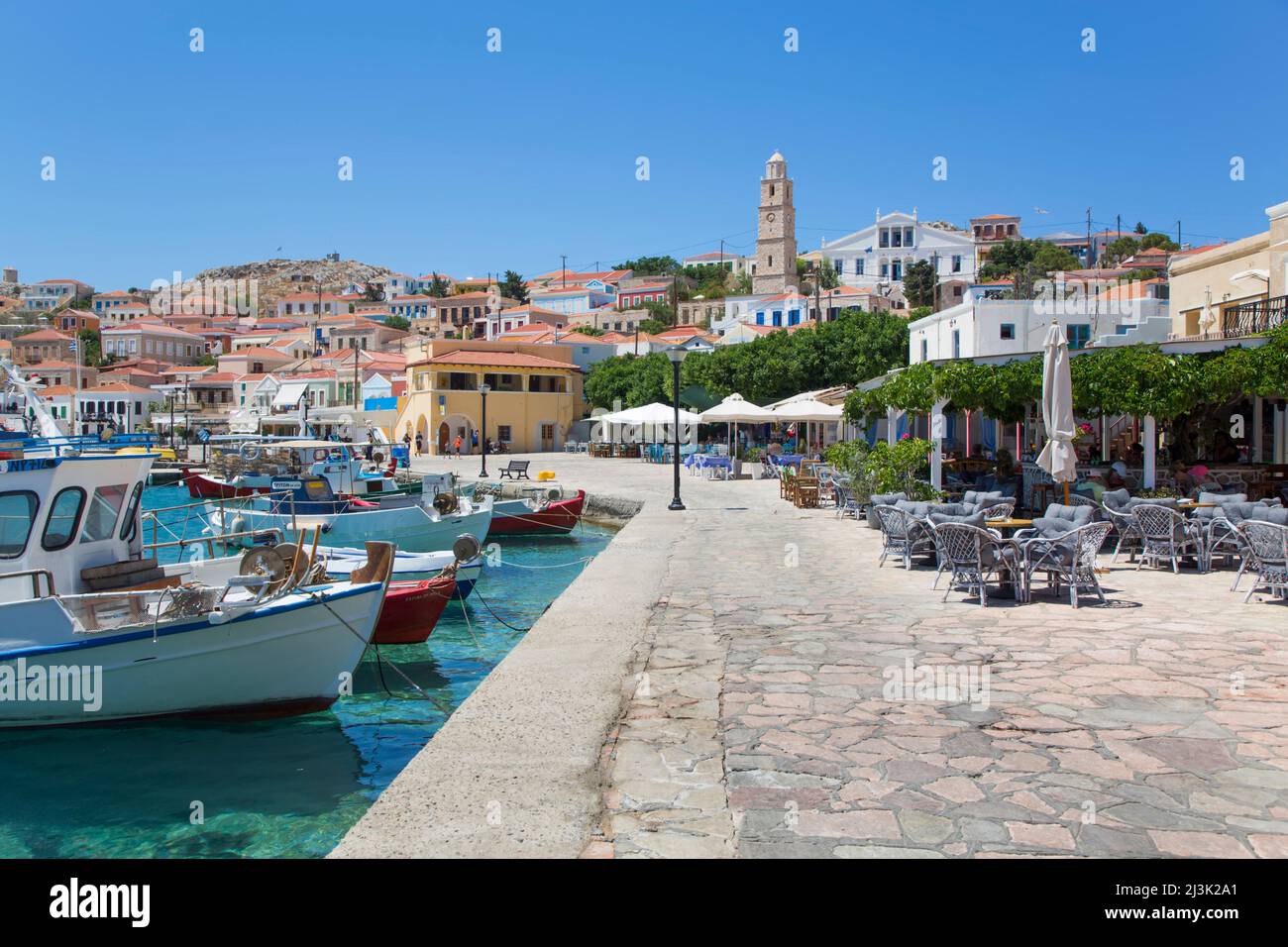 Barche ormeggiate e patio ristorante al porto di Emporio; Emporio, Halki, Dodecanese, Grecia Foto Stock