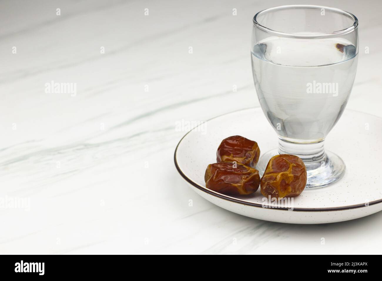 Kurma dan Air Putih, datteri di Sukkari e acqua su sfondo bianco marmo. Concetto di breakfasting nel mese del Ramadan. Modello islamico per lo sfondo del testo. Foto Stock