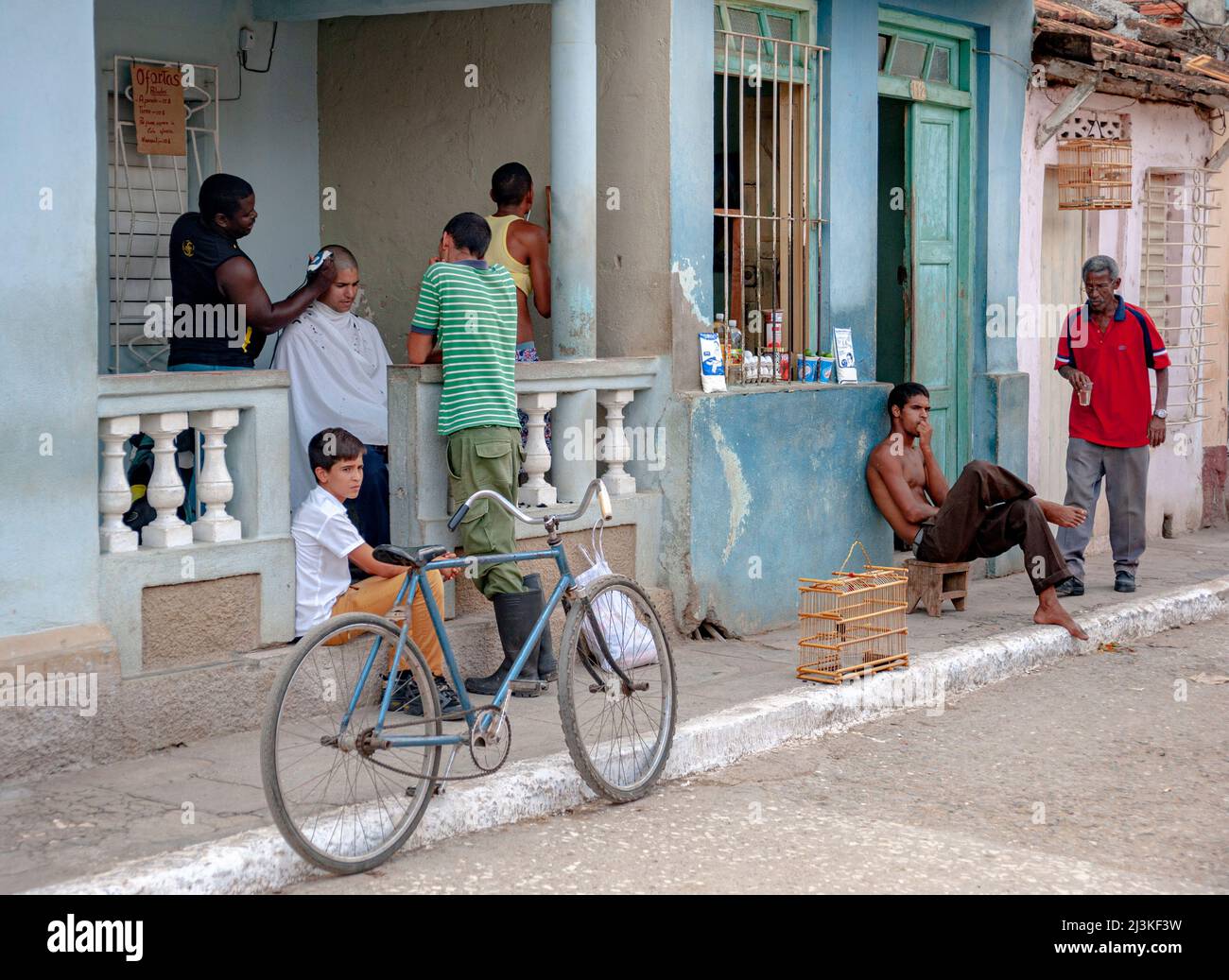Molte cose che accadono in un negozio di barbiere sul portico anteriore di una casa e vicino ad un negozio di alimentari di prodotti alimentari a Trinidad, Cuba. Foto Stock