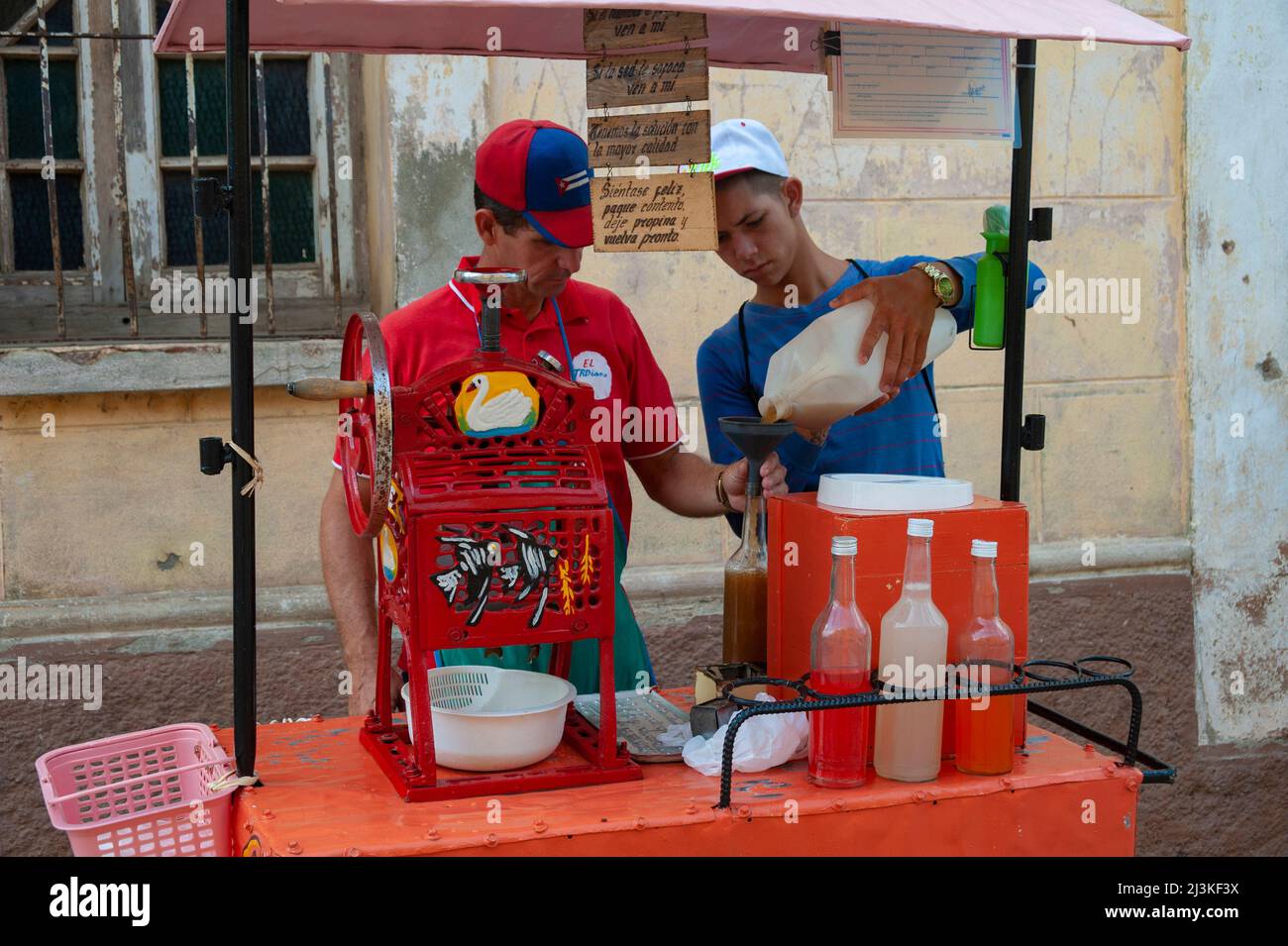 Due uomini cubani poveri una bevanda in una bottiglia per preparare i clienti in un caffè bevente a l'Avana, Cuba. Foto Stock