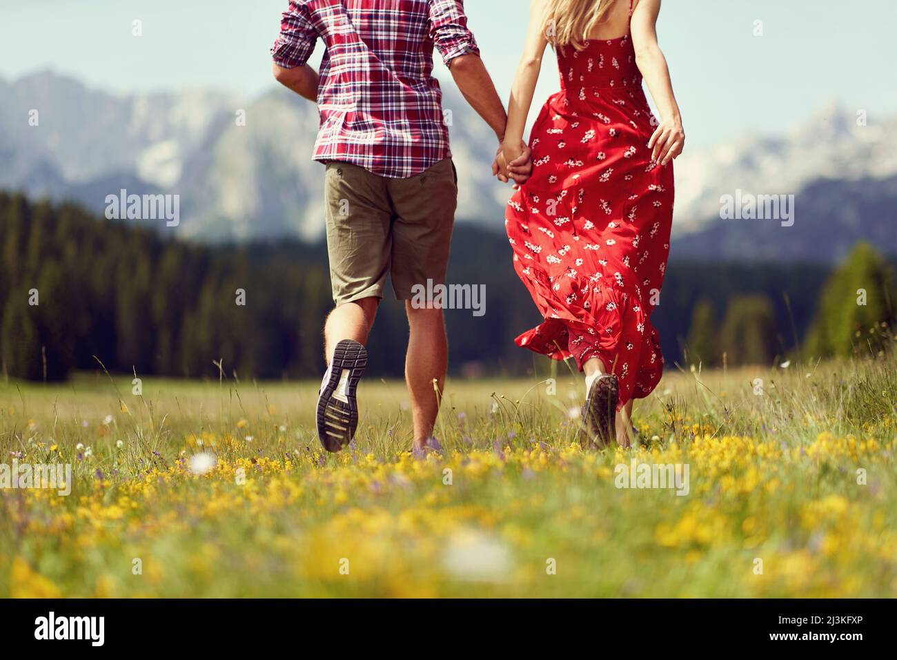 Vista posteriore della coppia che corre in prato verde. Divertimento, convivenza, stile di vita, concetto di natura. Foto Stock