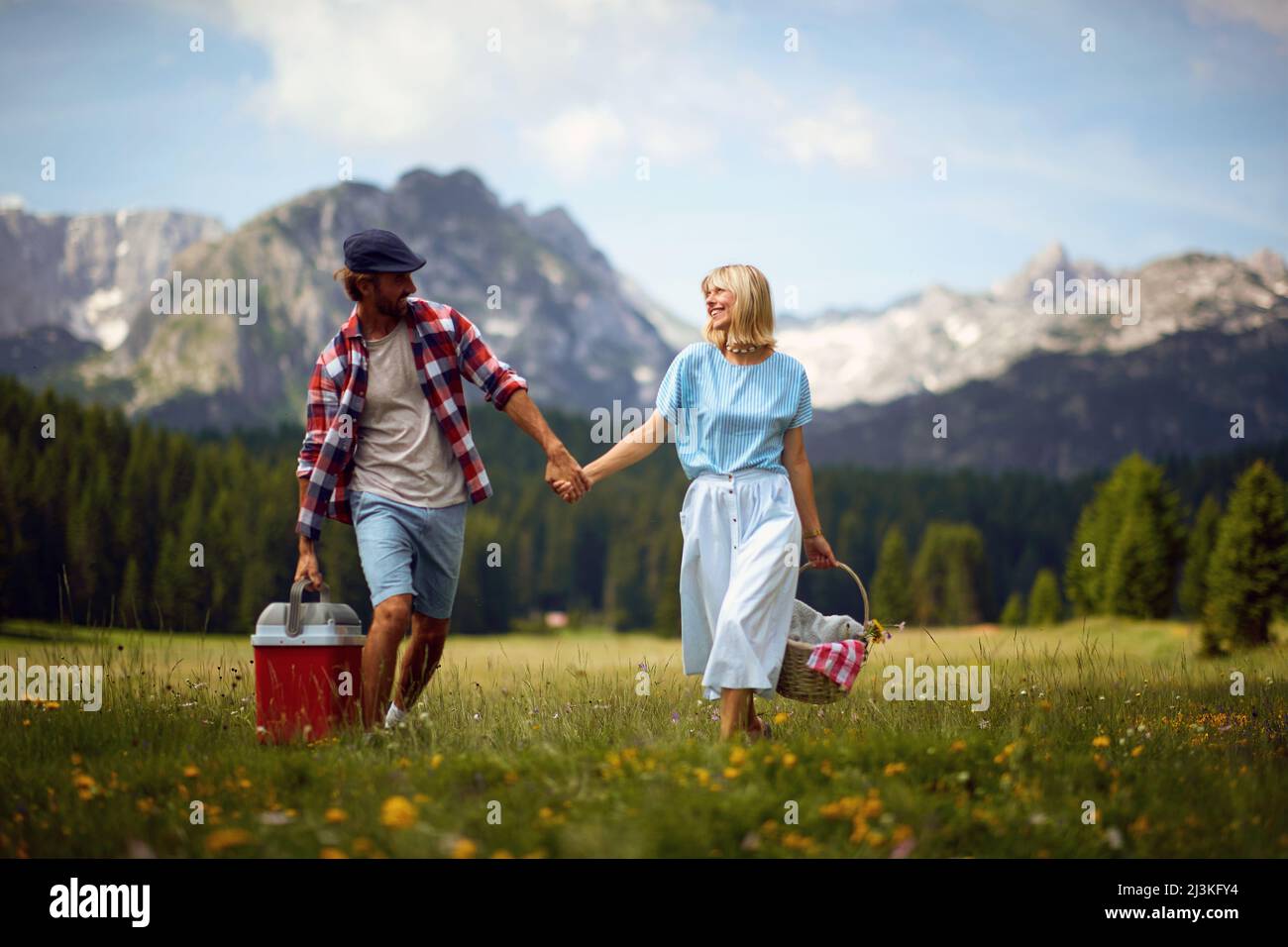 Uomo e donna che godono pic-nic in nature.Young allegro sorridente coppia in amore tenendo le mani e camminare nella natura in una bella giornata. Foto Stock