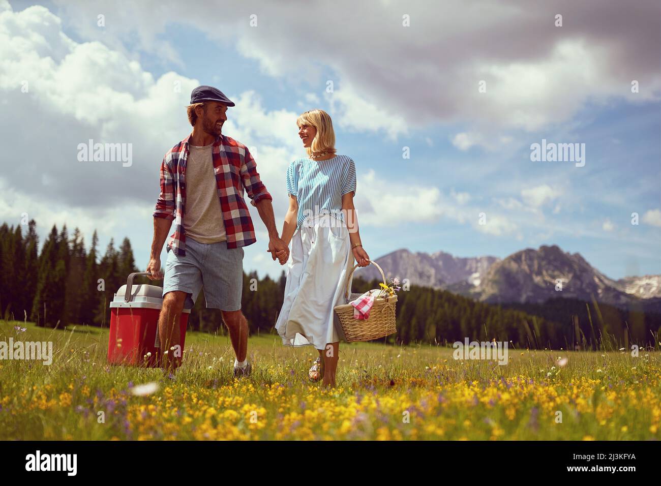 Giovane coppia sorridente e a piedi in natura con cesti da picnic. Divertimento, convivenza, stile di vita, concetto di natura. Foto Stock