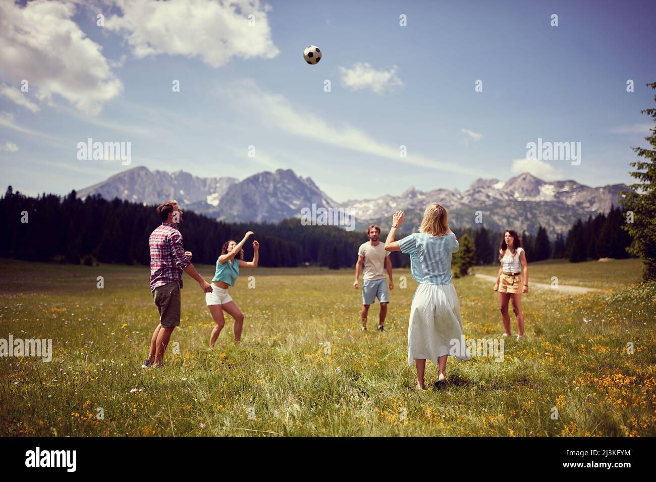 Gruppo di amici che si divertono a giocare con la palla sul prato verde. Godendo il tempo insieme nella natura. Divertimento, convivenza, stile di vita, concetto di natura. Foto Stock
