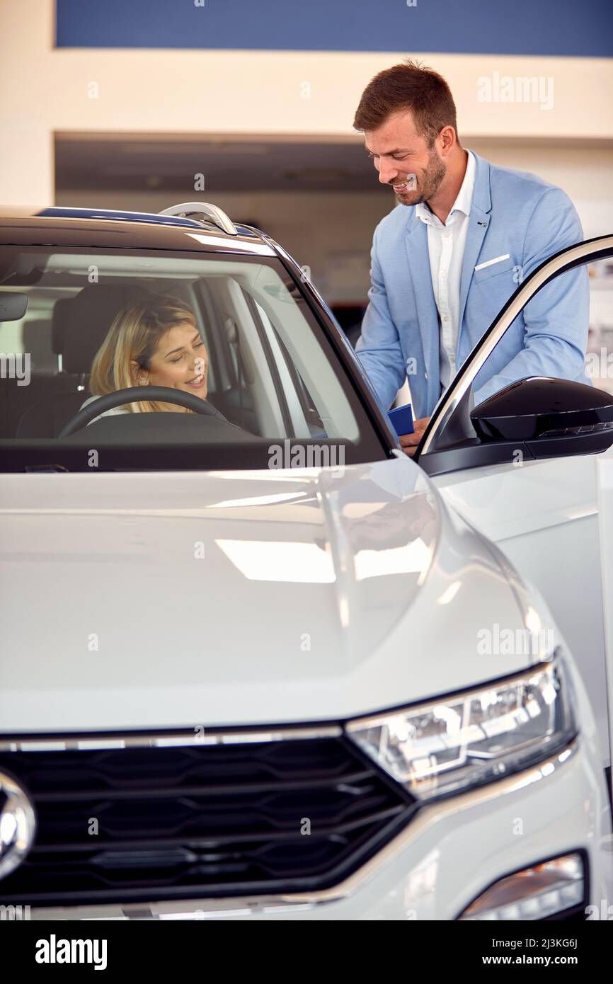 Donna seduta in una nuova auto in vendite auto salone e parlare con un venditore soddisfatto Foto Stock