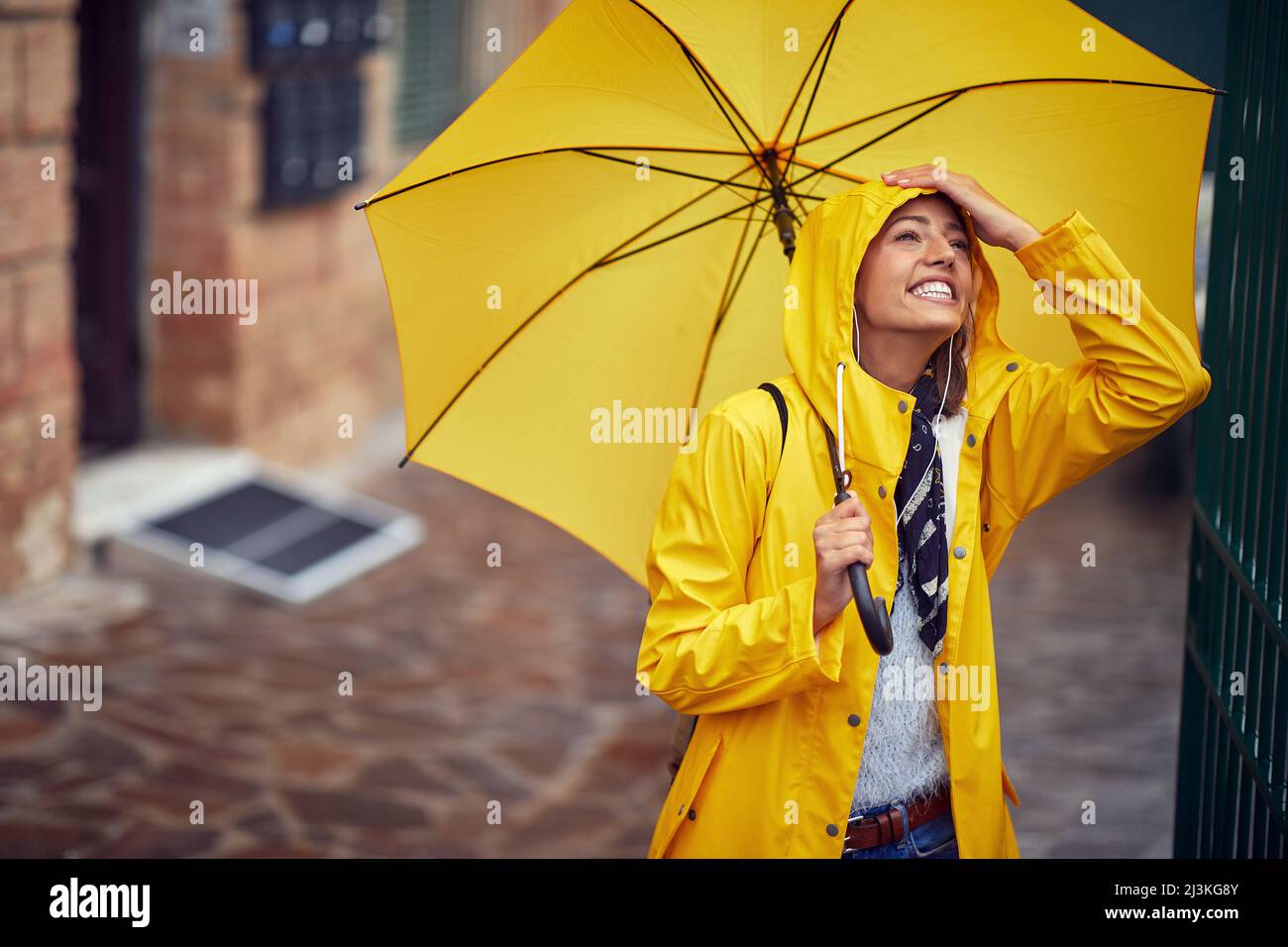 Una giovane donna allegra con un impermeabile giallo e un ombrello che è di buon umore mentre si cammina per la città in una giornata piovosa in modo rilassato. Cammina, pioggia Foto Stock