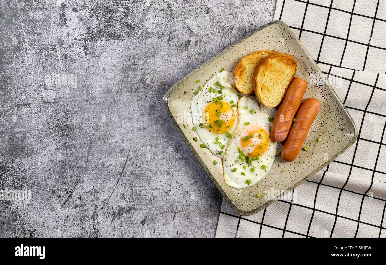 Colazione semplice: Uova fritte e salsicce con toast su un piatto quadrato su sfondo scuro. Vista dall'alto, piatto Foto Stock