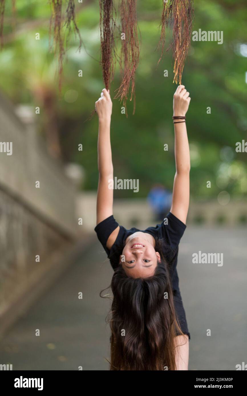 La ragazza della premea raggiunge fino a tenere le viti e guarda la macchina fotografica da capovolto; Hong Kong, Cina Foto Stock