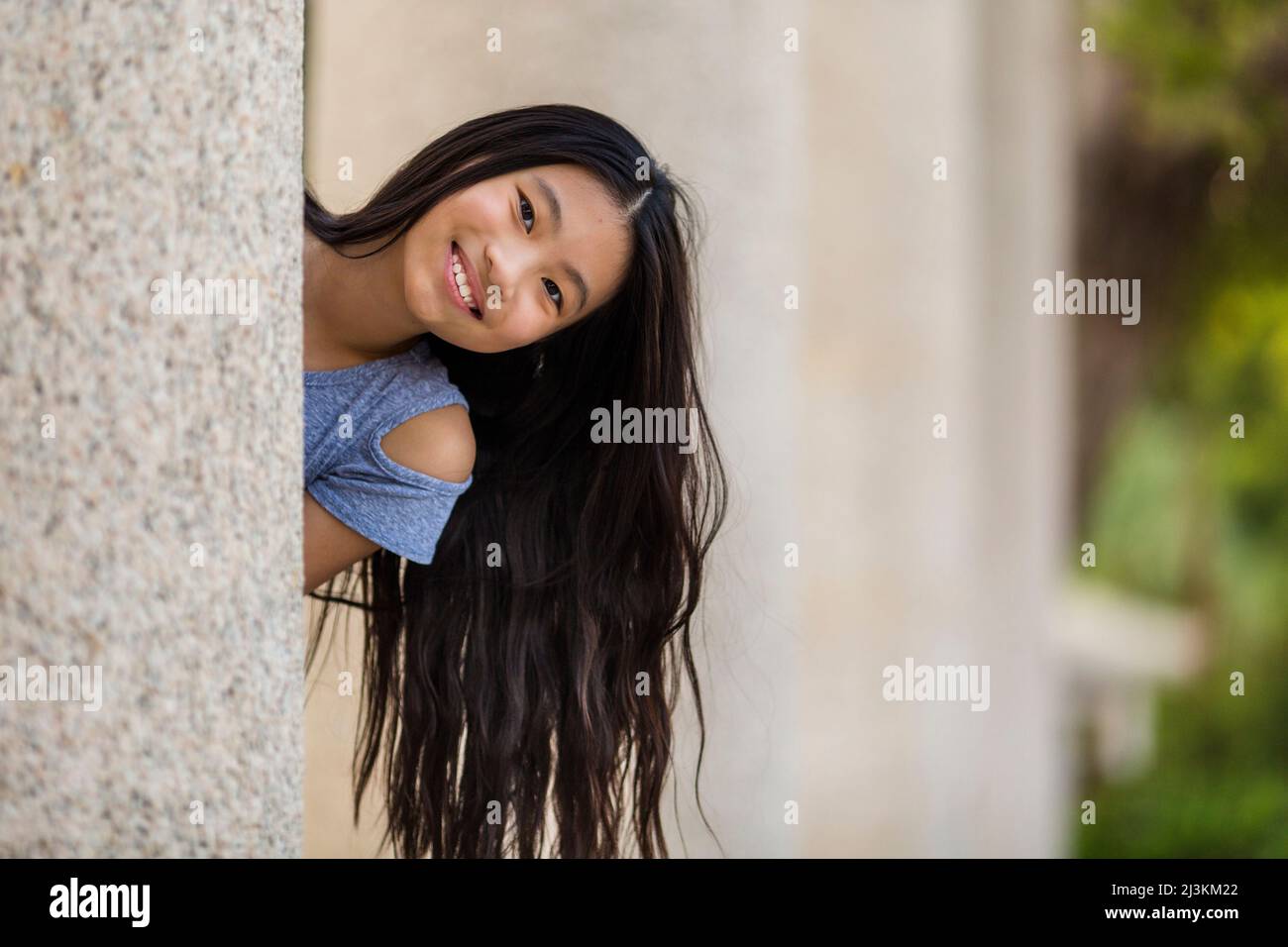 Ritratto all'aperto di una ragazza con capelli lunghi e scuri come lei guarda fuori da dietro la parete alla macchina fotografica; Stanley, Hong Kong, Cina Foto Stock