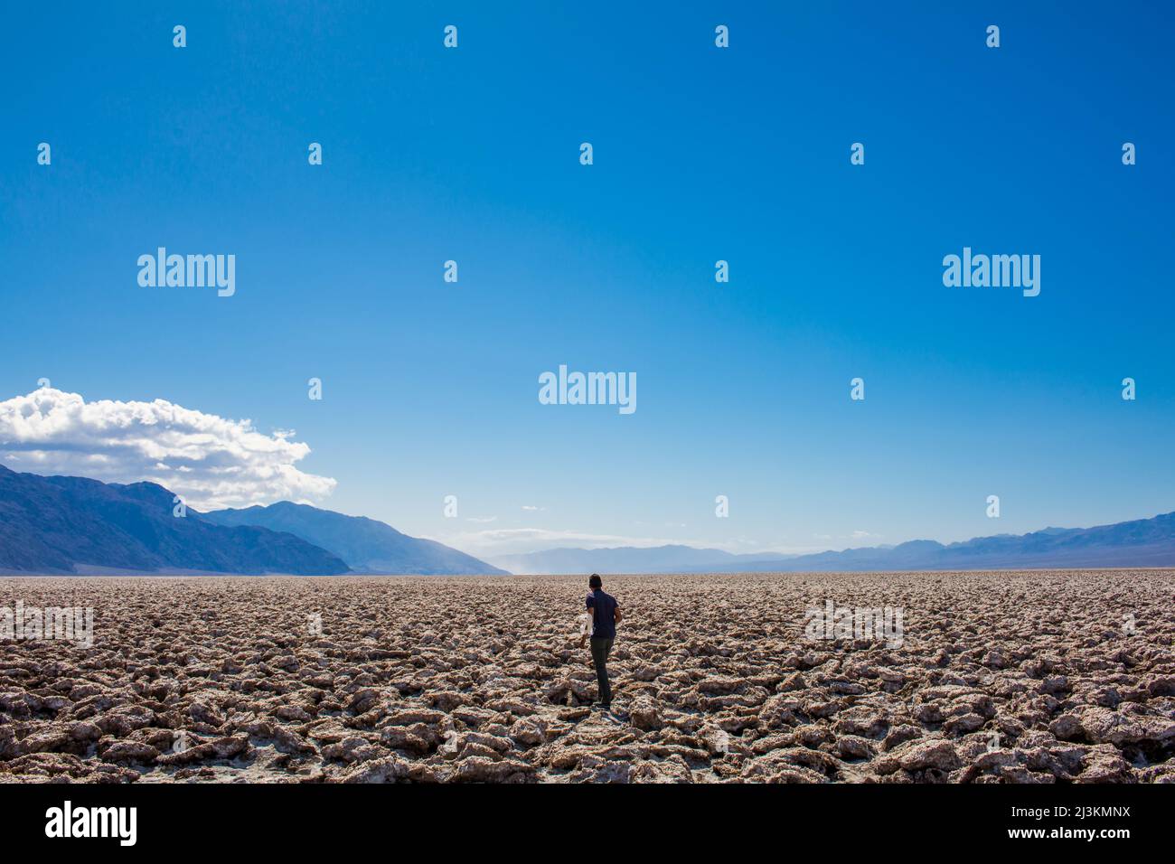 Un uomo a piedi attraverso il deserto incrinato pianure nella Valle della Morte. Foto Stock