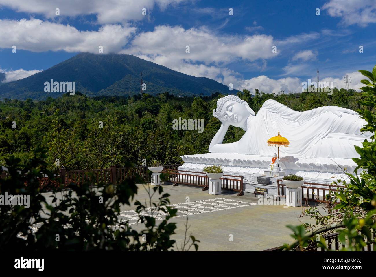 Statua bianca del buddha dormiente in una posa distesa con una montagna e gli alberi sullo sfondo, il tempio di Vihara Dharma Giri; Tabanan, Bali, Indonesia Foto Stock