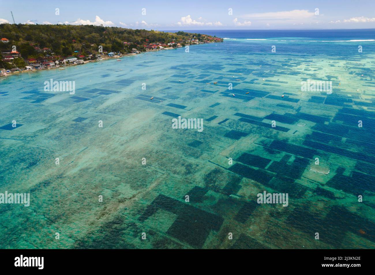 Antenna della via d'acqua tra Nusa Lembongan e Nusa Ceningan mostrando piccole barche ormeggiate sulla cima delle zone subacquee di alghe fa... Foto Stock