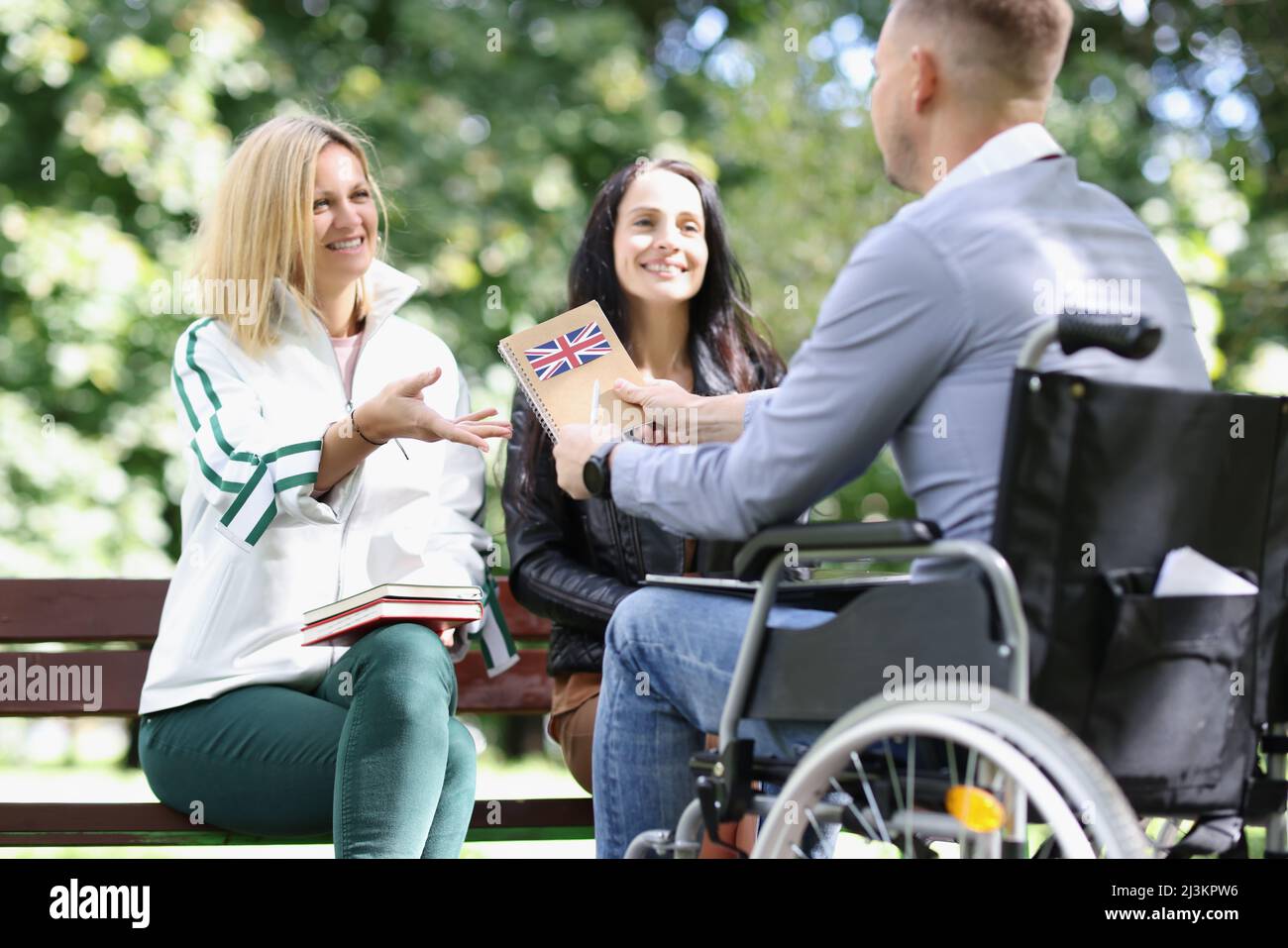 Due donne e un uomo in sedia a rotelle imparano l'inglese mentre si siedono nel parco Foto Stock