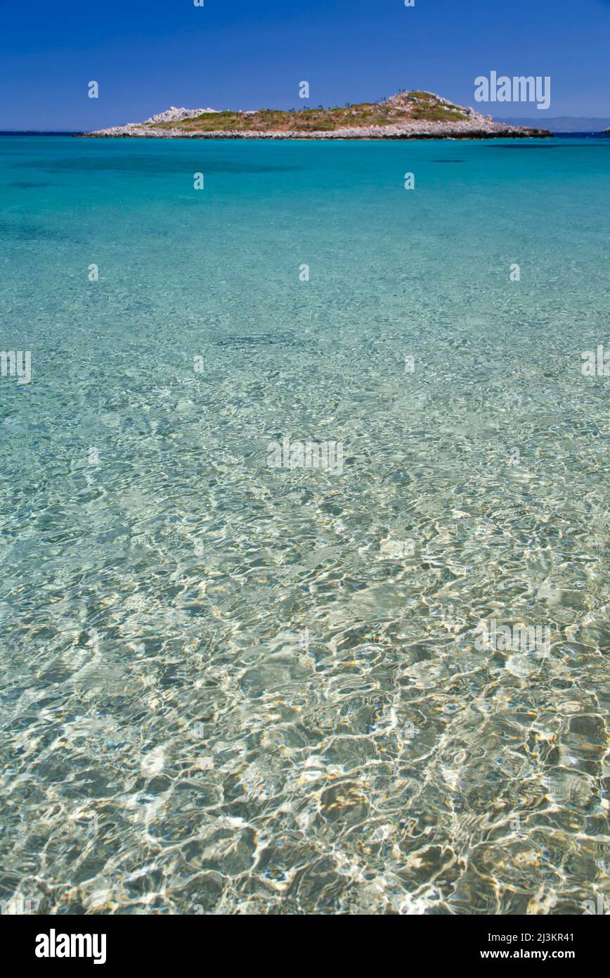 Isoletta con cielo blu e acqua cristallina dell'oceano, vicino alla spiaggia di Sesklia, all'isola di Symi (Simi), al gruppo dell'isola del Dodecaneso in Grecia; all'isola di Symi, in Grecia Foto Stock
