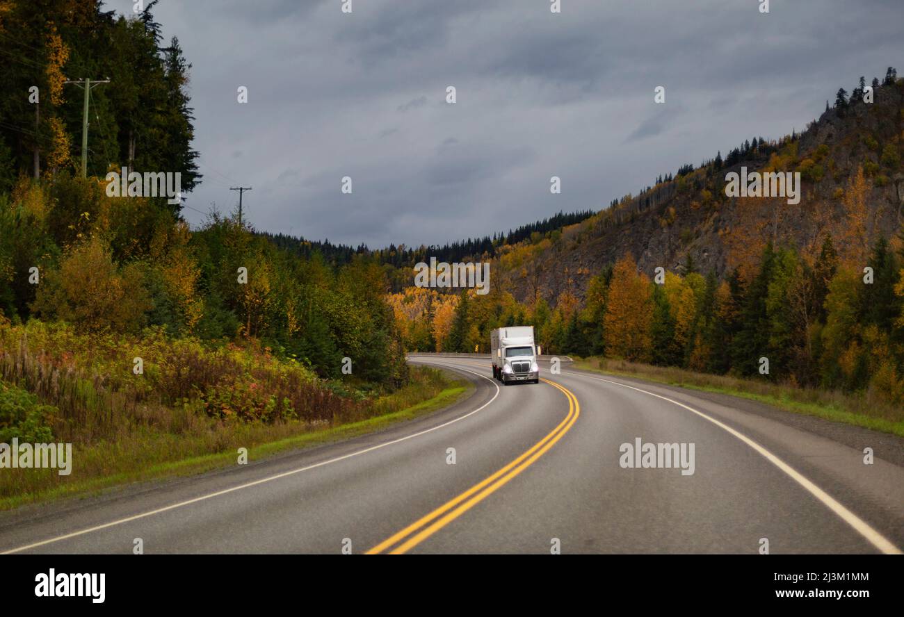 Trasporto camion viaggiando sull'autostrada 16 con alberi di colore autunnale lungo la strada; British Columbia, Canada Foto Stock