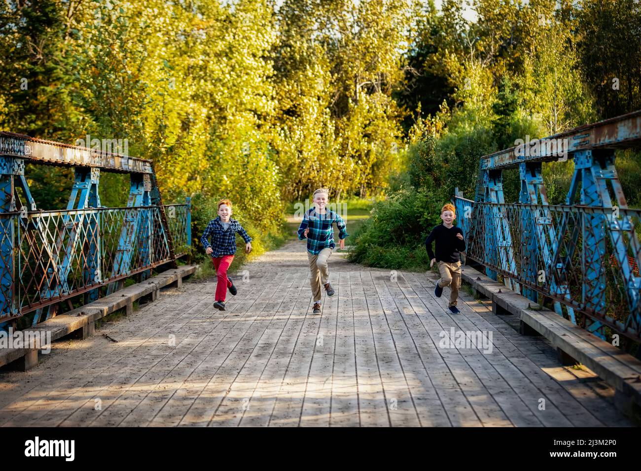 Tre ragazzi che corrono attraverso un ponte in un parco in autunno; Edmonton, Alberta, Canada Foto Stock