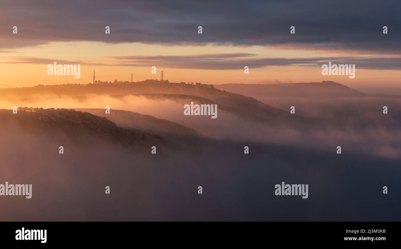 Il tramonto illumina una riva di nebbia gelida mentre si riversa sulle colline del South Downs National Park; Brighton, East Sussex, Inghilterra Foto Stock