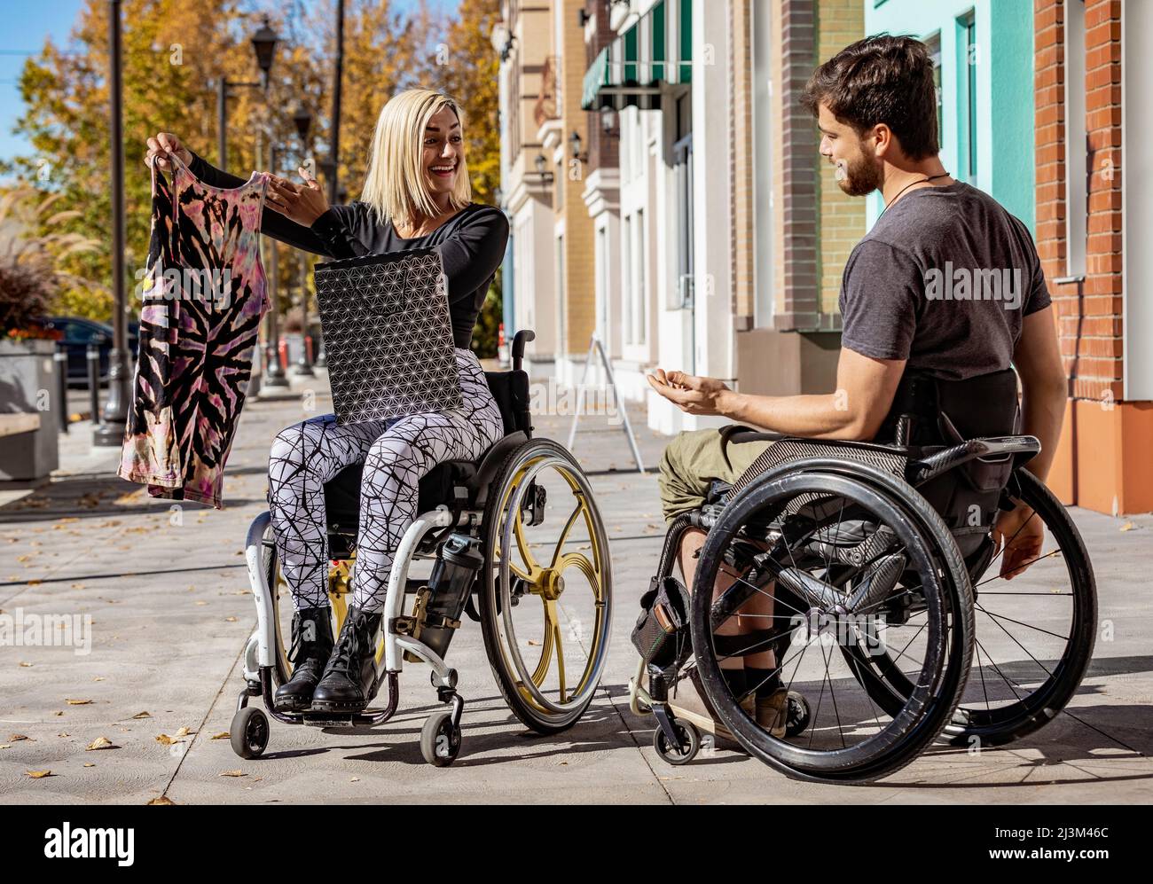 Giovani amici paraplegici che trascorrono tempo insieme all'esterno mentre si fa shopping in una zona della città, ragazza chiedendo al suo ragazzo per la sua opinione su un acquirente... Foto Stock