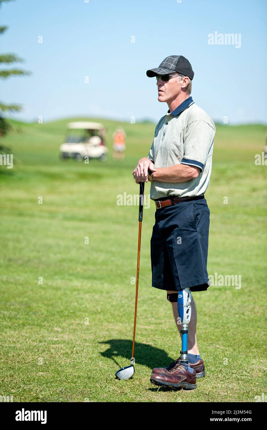 Amputee con protesi per le gambe in piedi con golf club sul campo; Okotoks, Alberta, Canada Foto Stock