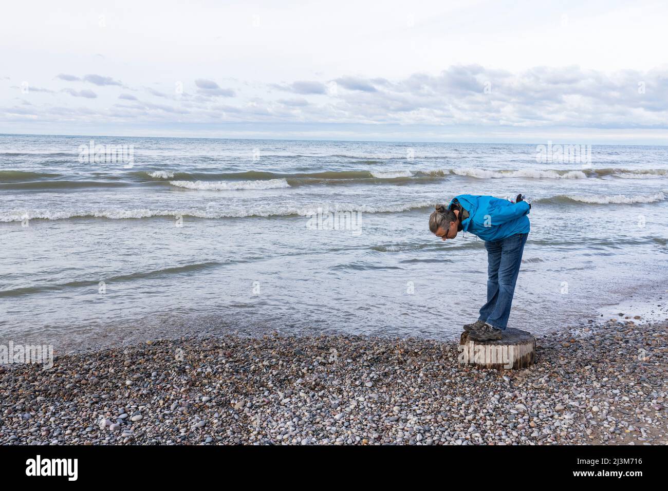 Uomo che guarda le rocce costiere del lago Huron mentre le onde rotolano in; Grand Bend, Ontario, Canada Foto Stock