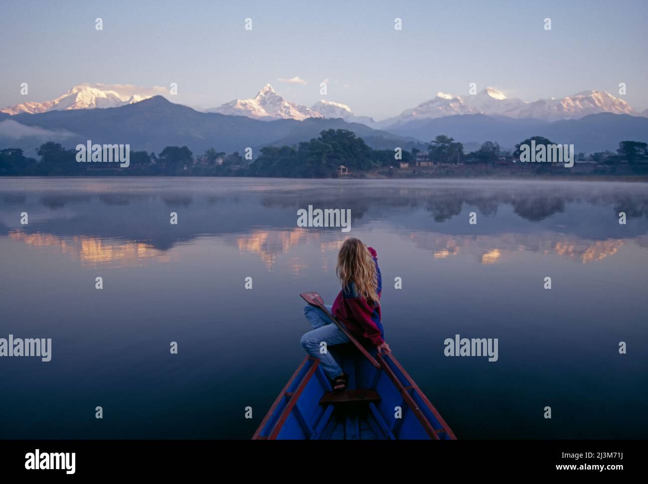 Una donna in un gazes della barca a remi alla gamma di Annapurna all'alba.; gamma di Annapurna, montagne di Himalaya, Nepal. Foto Stock