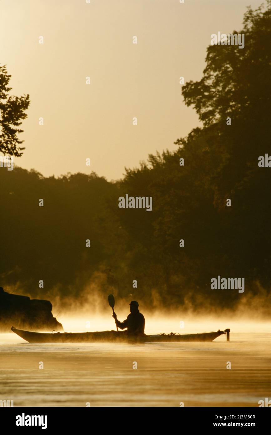 Un kayak pagaia attraverso la nebbia che si alza dal fiume Potomac all'alba.; Potomac fiume, Maryland. Foto Stock