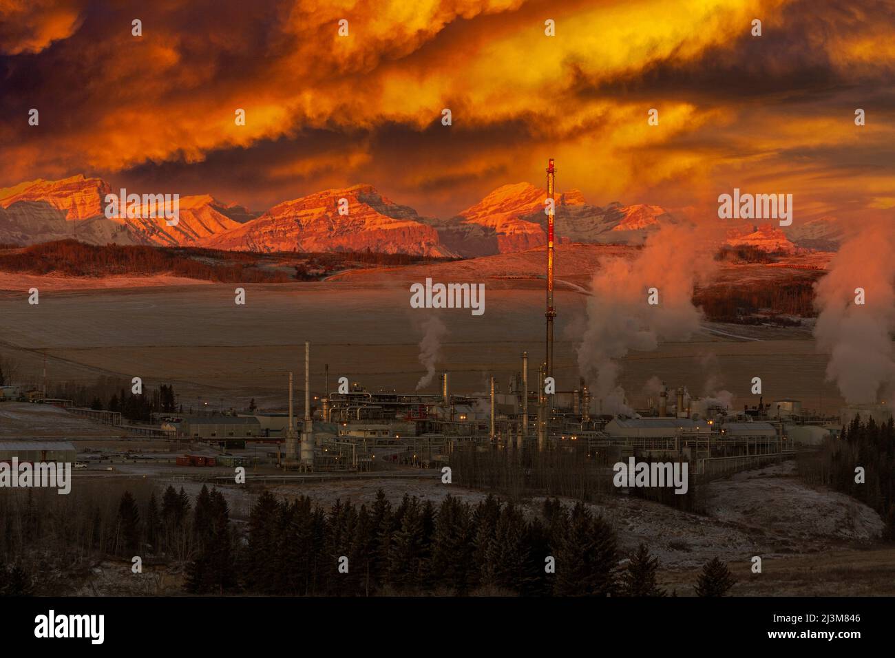Impianto a gas drammaticamente lite all'alba con la catena montuosa ricoperta di neve sullo sfondo con le nuvole incandescenti nel cielo, ad ovest di Calgary Foto Stock