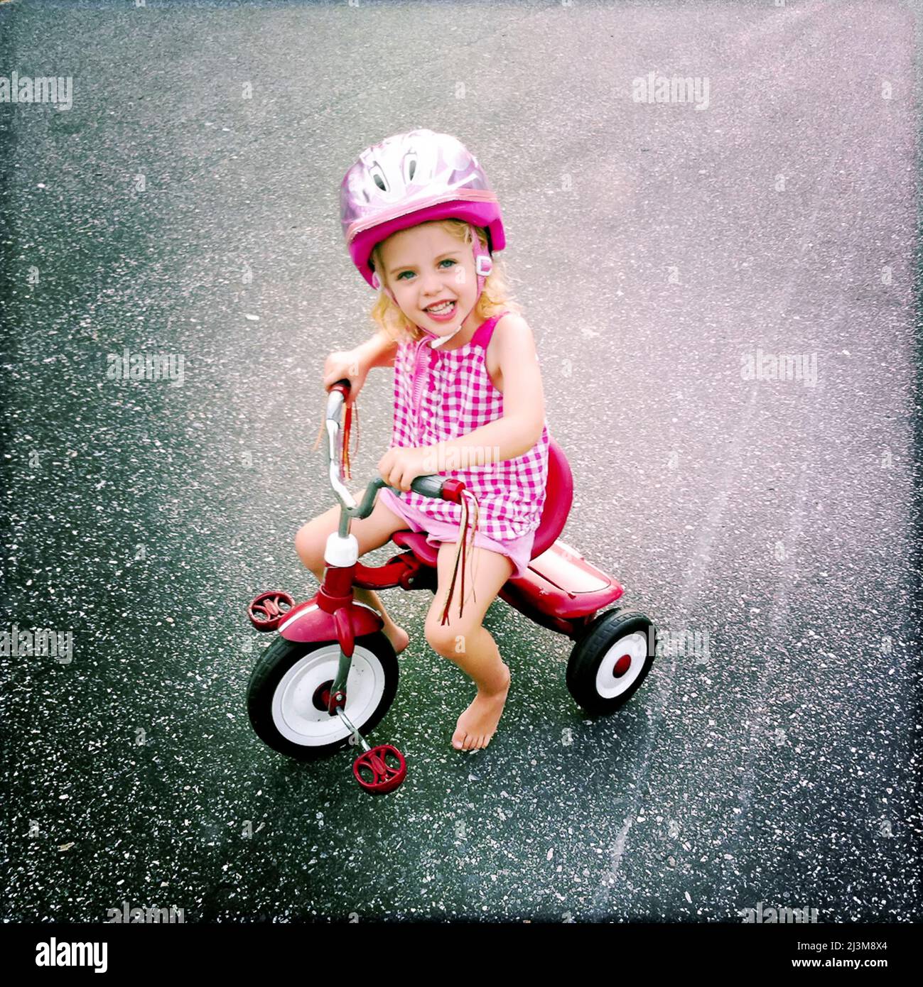 Una bambina di due anni corre il suo triciclo di corsa in un giorno d'estate.; Cabin John, Maryland, Stati Uniti. Foto Stock