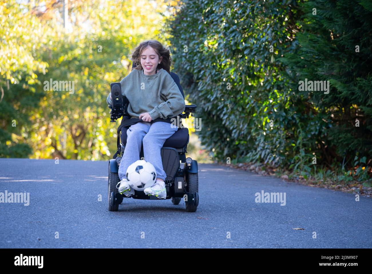 Ragazza di undici anni con Ullrich muscoloso distrofia congenita gioca il calcio nella sua sedia a rotelle vicino a casa sua Foto Stock