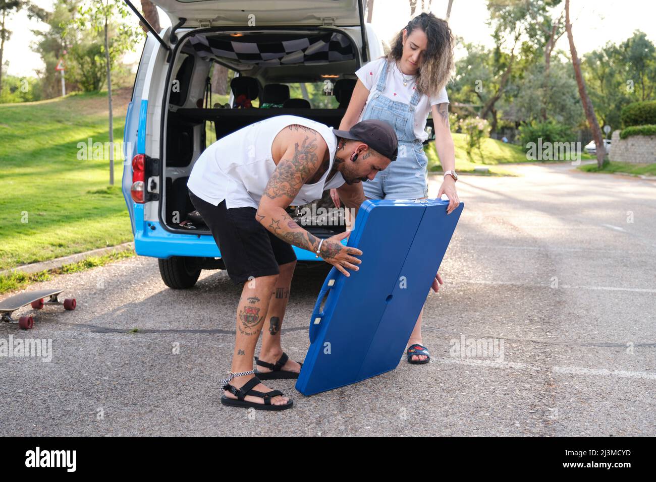 Giovane coppia tatuata mettendo tavolo da picnic montaggio vicino al furgone. Foto Stock