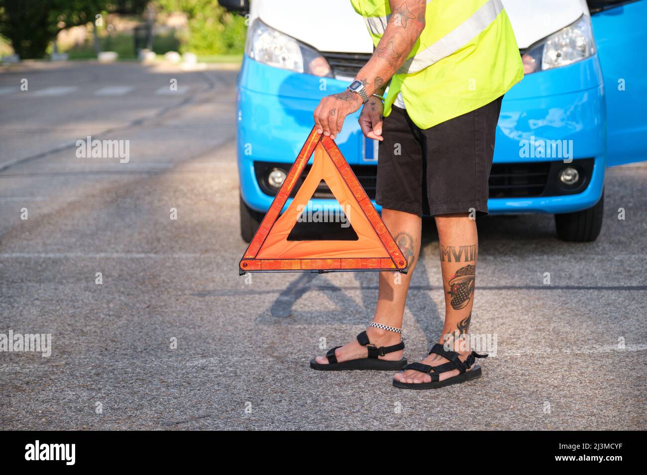 L'uomo tatuato irriconoscibile posiziona un triangolo di sicurezza riflettente davanti al suo furgone. Foto Stock