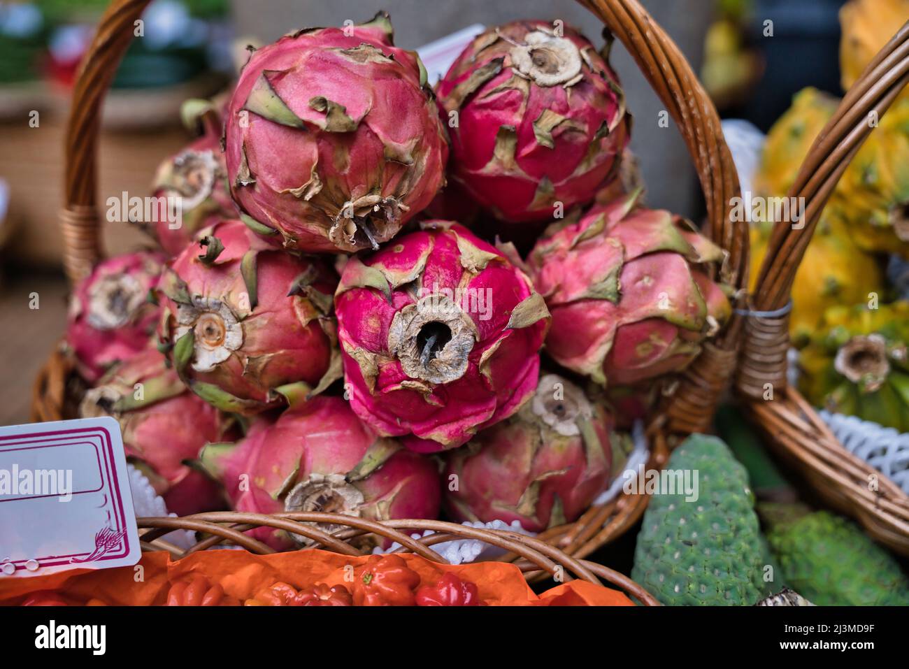 Un cesto in tessuto riempito di melagrane in un mercato a Funchal, Madeira. Altri frutti possono essere visti sullo sfondo. Foto Stock