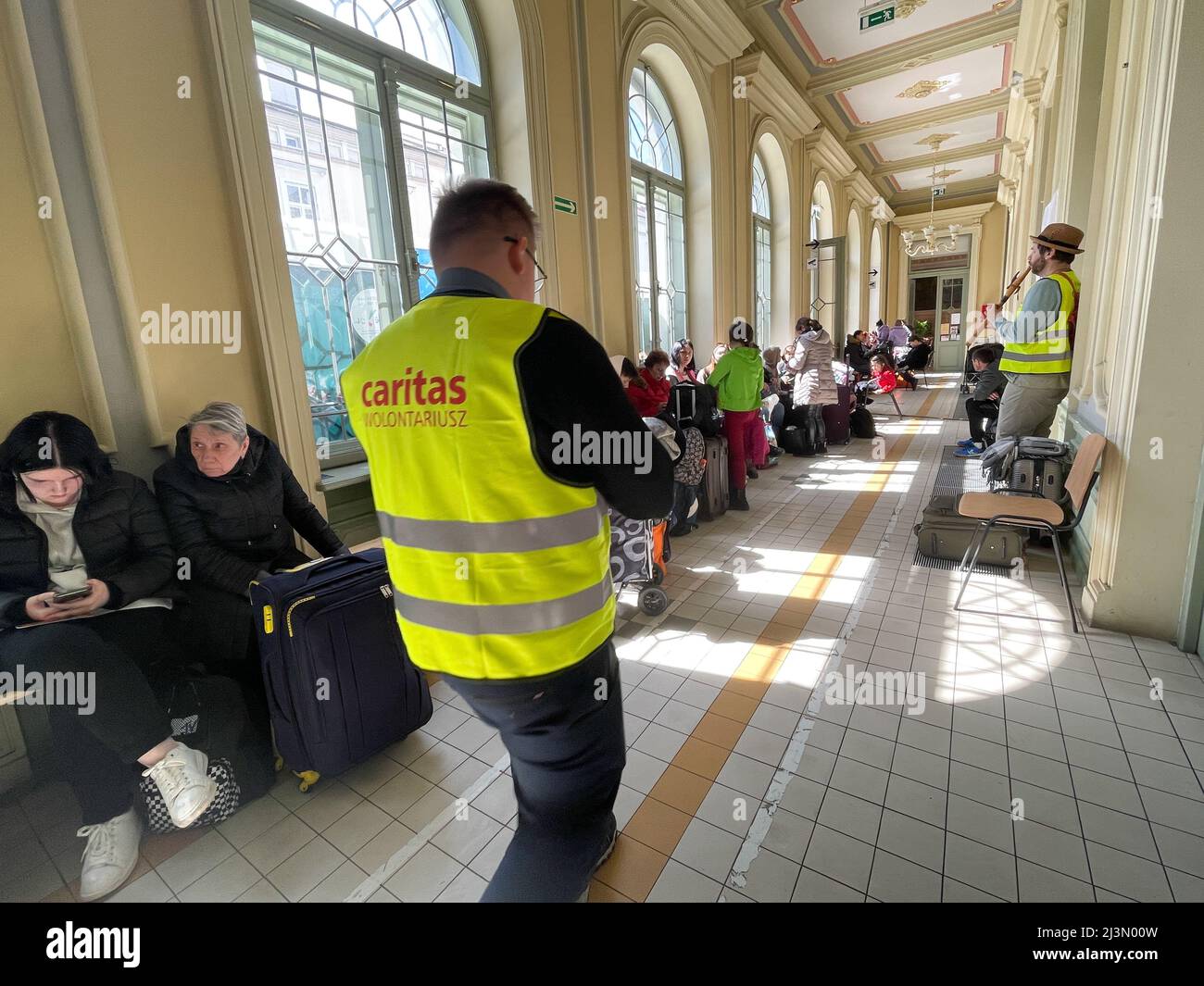 Przemysl, Polonia. 8th Apr 2022. Un volontario della Caritas attraversa il corridoio pieno di rifugiati ucraini, come Fabian, un volontario francese compassionevole e soulful che ha praticato il buddismo per oltre 20 anni, gioca il suo flauto per cercare di sollevare gli spiriti degli ucraini devastati dalla guerra di Putin, che formano lunghe code sui banchi rigidi dove molti attenderanno molte ore, in attesa di salire a bordo di treni che li allontaneranno dal terrore che hanno vissuto per la sicurezza di nuove case. (Credit Image: © Amy Katz/ZUMA Press Wire) Credit: ZUMA Press, Inc./Alamy Live News Foto Stock