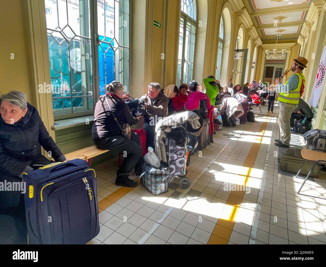 Przemysl, Polonia. 8th Apr 2022. Un volontario della Caritas attraversa il corridoio pieno di rifugiati ucraini, come Fabian, un volontario francese compassionevole e soulful che ha praticato il buddismo per oltre 20 anni, gioca il suo flauto per cercare di sollevare gli spiriti degli ucraini devastati dalla guerra di Putin, che formano lunghe code sui banchi rigidi dove molti attenderanno molte ore, in attesa di salire a bordo di treni che li allontaneranno dal terrore che hanno vissuto per la sicurezza di nuove case. (Credit Image: © Amy Katz/ZUMA Press Wire) Credit: ZUMA Press, Inc./Alamy Live News Foto Stock