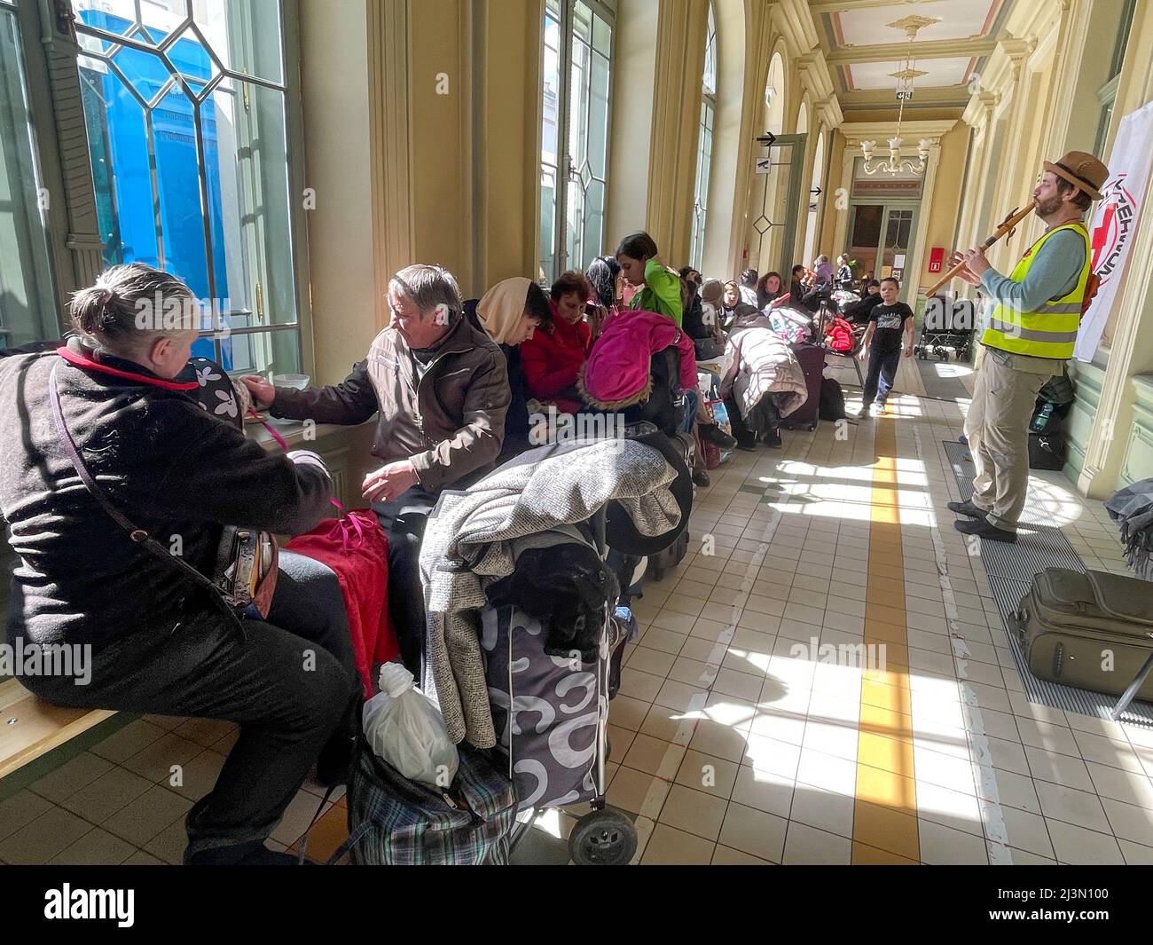 Przemysl, Polonia. 8th Apr 2022. Un volontario della Caritas attraversa il corridoio pieno di rifugiati ucraini, come Fabian, un volontario francese compassionevole e soulful che ha praticato il buddismo per oltre 20 anni, gioca il suo flauto per cercare di sollevare gli spiriti degli ucraini devastati dalla guerra di Putin, che formano lunghe code sui banchi rigidi dove molti attenderanno molte ore, in attesa di salire a bordo di treni che li allontaneranno dal terrore che hanno vissuto per la sicurezza di nuove case. (Credit Image: © Amy Katz/ZUMA Press Wire) Credit: ZUMA Press, Inc./Alamy Live News Foto Stock