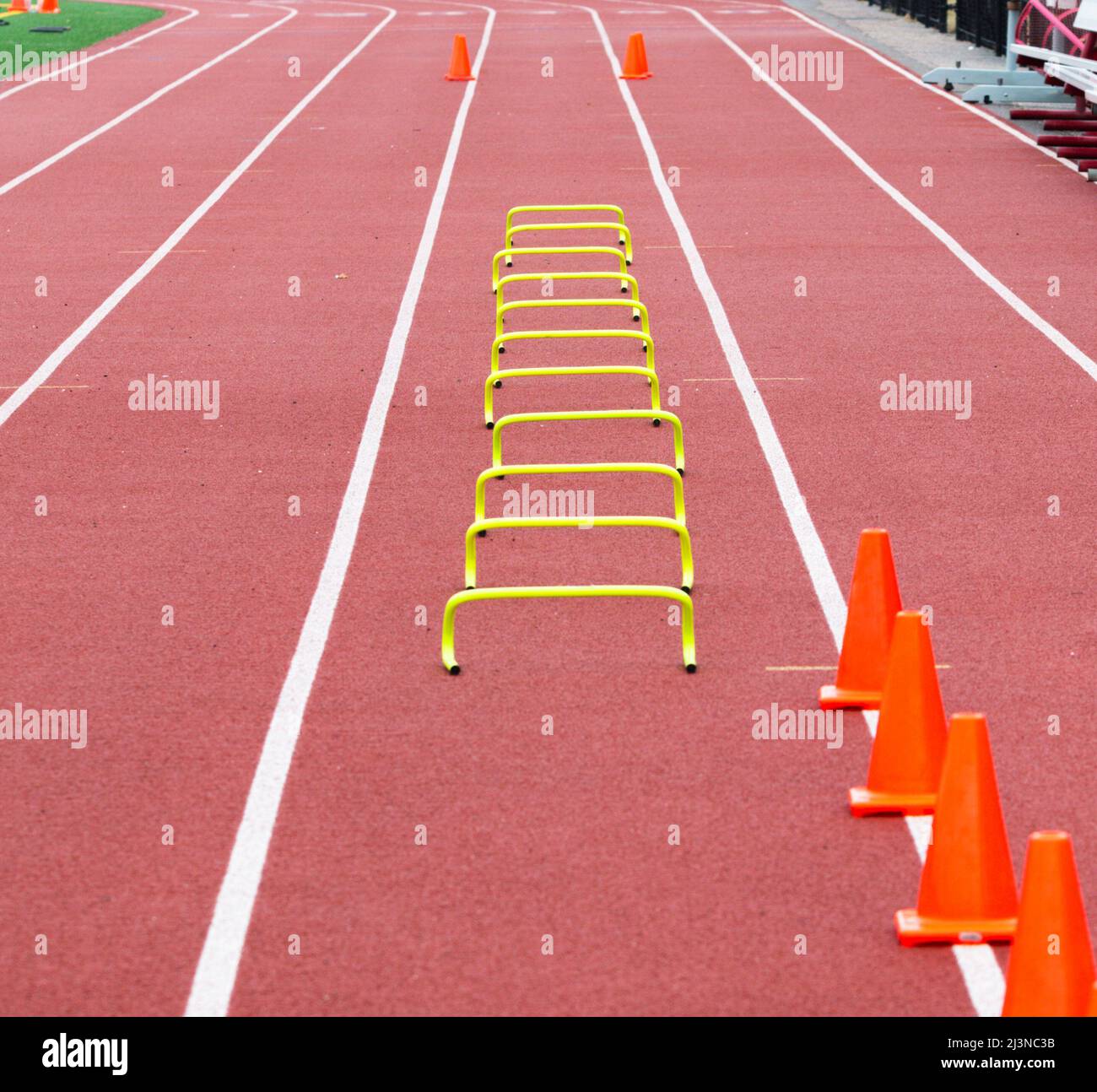 Undici ostacoli di plastica gialli alti sei pollici sistemati nella corsia quattro per lo sprinter della scuola superiore per correre sopra con coni arancioni nella distanza che contrassegna la pinna Foto Stock