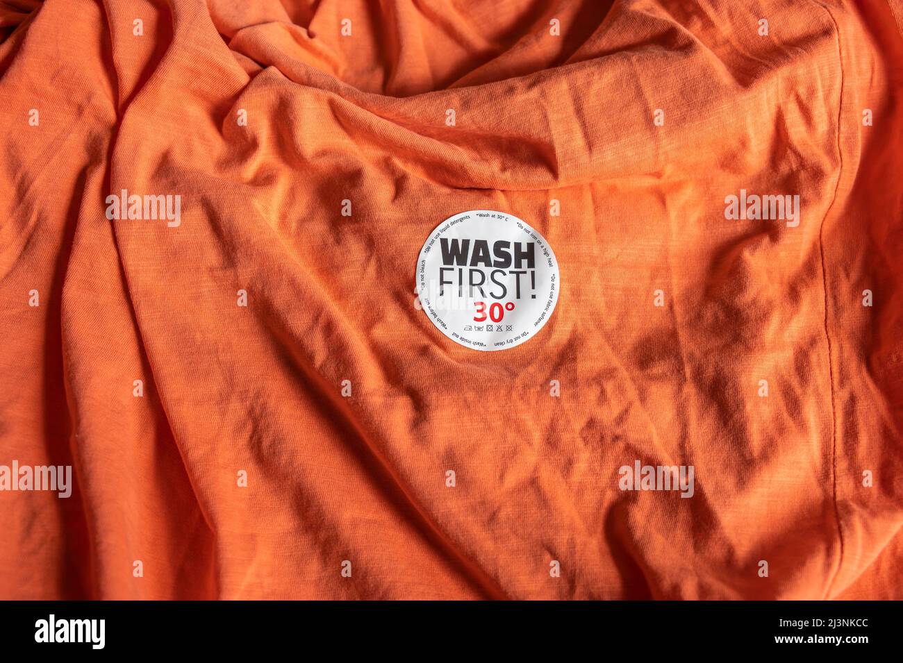 Adesivo su una T-shirt con istruzioni per il lavaggio e il testo "Lavare prima". Foto Stock