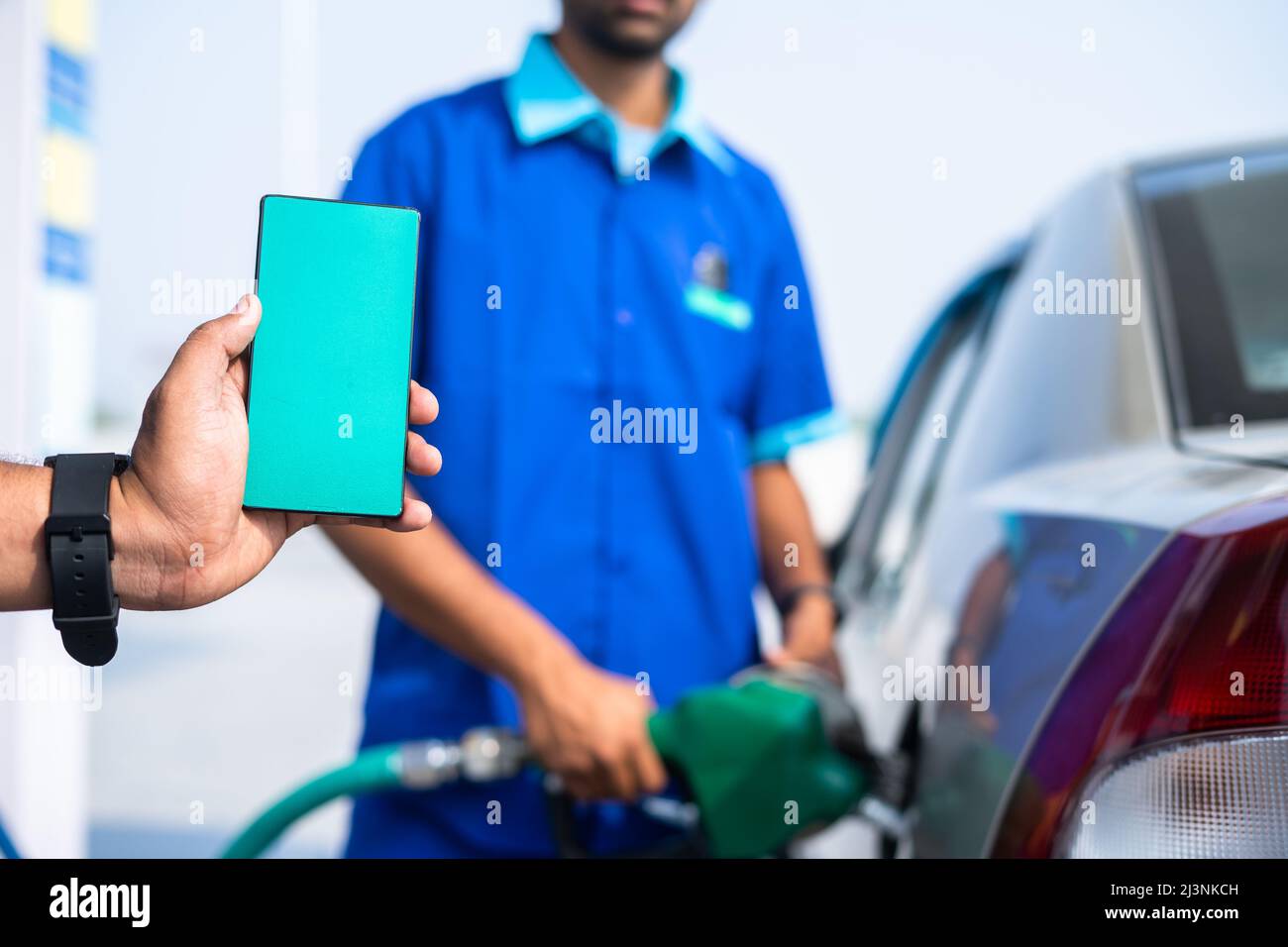 primo piano di mano che mostra il telefono cellulare con schermo verde mentre il lavoratore che riempie benzina su auto - concetto di applicazione di pubblicità, promozione e. Foto Stock