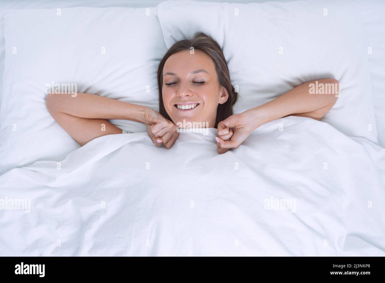 Buongiorno. Vista dall'alto della bella giovane donna che si svegliava felice nel letto bianco. Giorno fuori dal lavoro Foto Stock