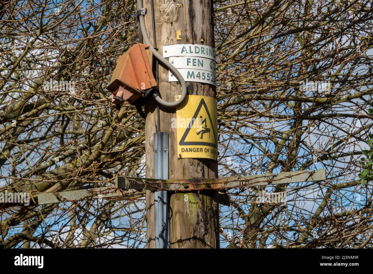 Un segnale di pericolo di morte montato su un palo di legno sopra un'unità di filo metallico e spinato per scoraggiare l'arrampicata Foto Stock