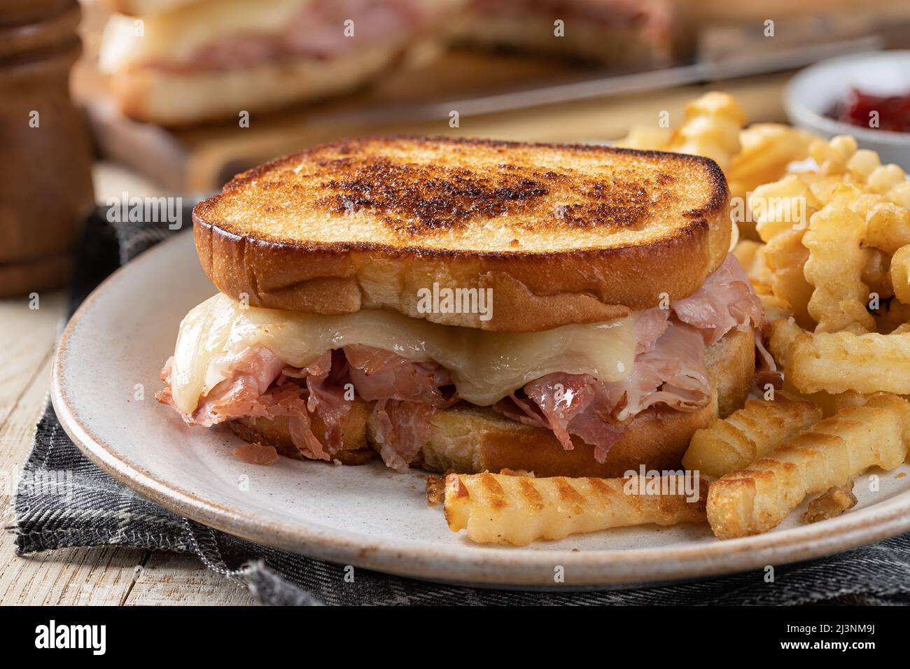 Primo piano di un sandwich di prosciutto e formaggio alla griglia e patatine fritte su un piatto Foto Stock
