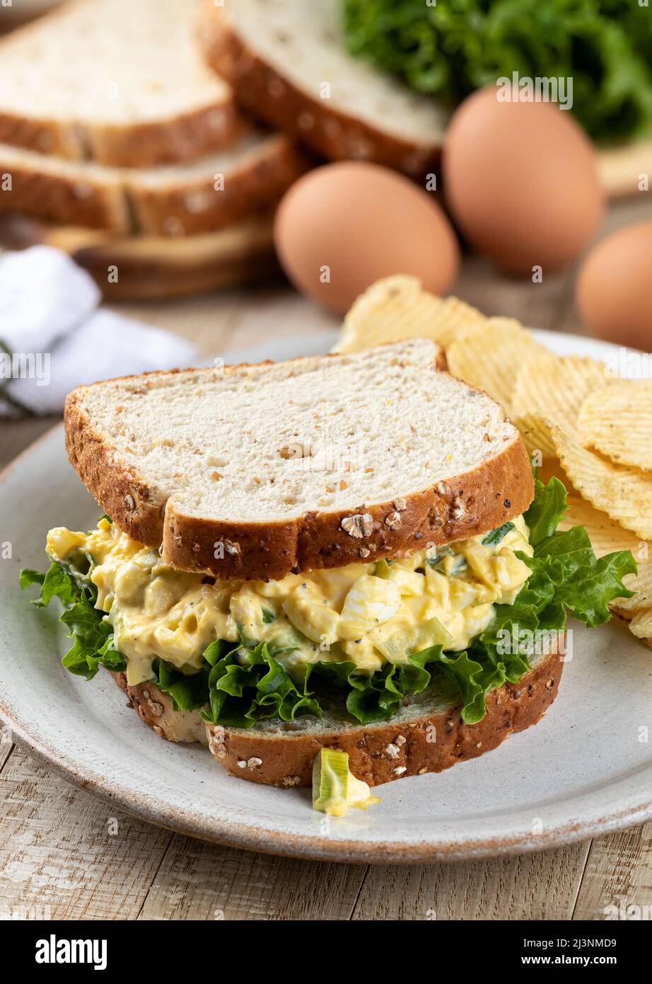 Sandwich con insalata di uova e lattuga su pane intero con patatine su un piatto Foto Stock